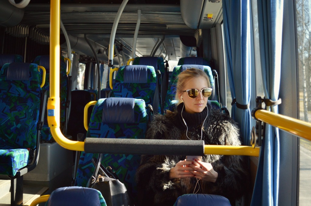 Nuori naismatkustaja istuu bussissa aurinkolasit silmillä ja kuulokkeet korvilla.