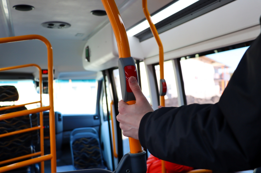 Kuvassa ihminen painaa sormella bussin stop-painiketta.