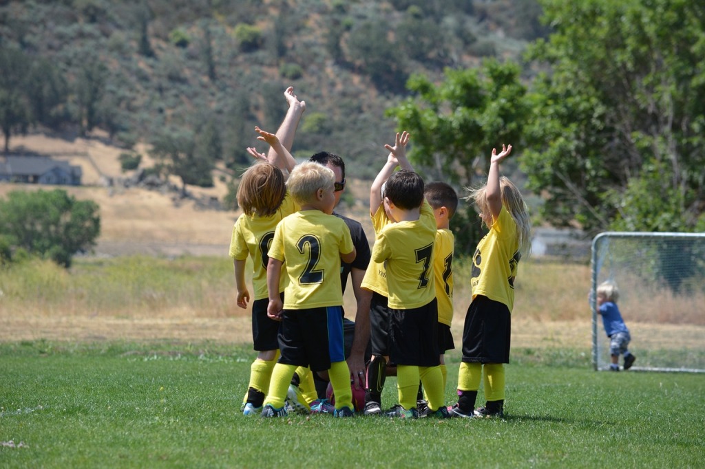 Kuvassa pienten lasten ryhmä jalkapallokentällä keltamustissa peliasuissaan.
