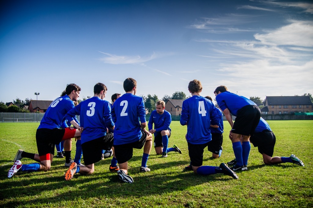 Aikuisten miesten jalkapallojoukkue kokoontunut ryhmään keskustelemaan kentällä sinimustissa peliasuissa.